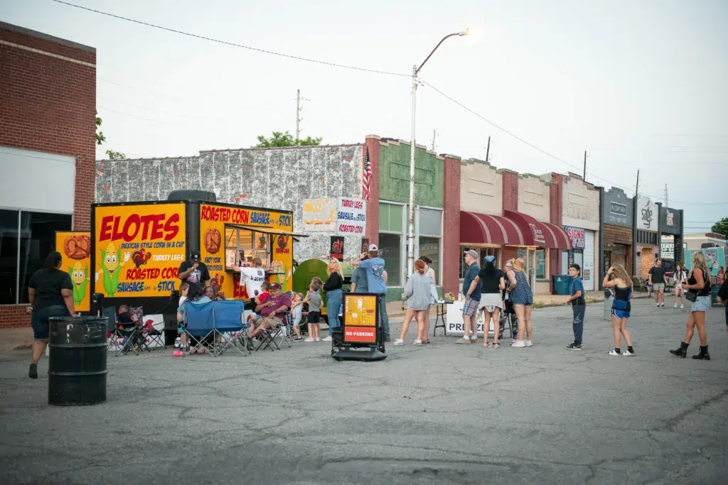 Festival attendees browse vendor stands and food carts in an outdoor street venue with historic brick buildings.