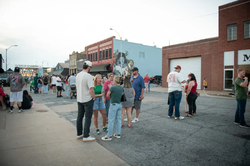 Festival attendees gather in a downtown street surrounded by brick buildings and colorful murals.