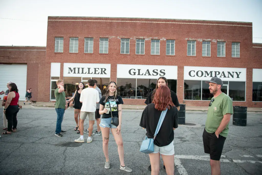 Festival attendees gather in a parking lot in front of the Miller Glass Company building.