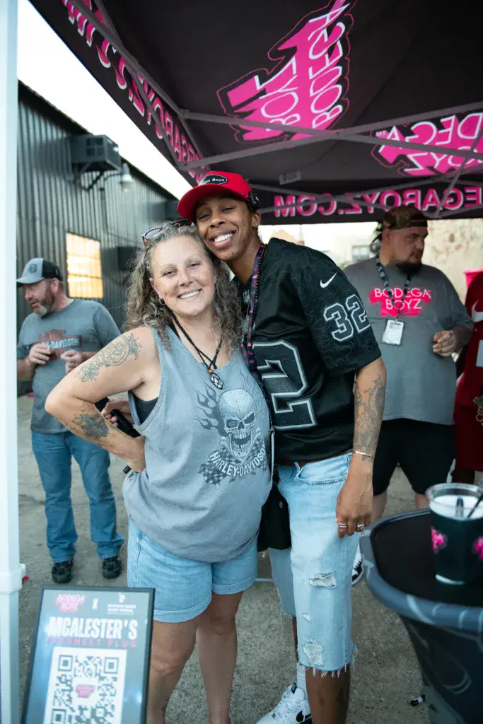 Two people smile together at the Dancing Rabbit Music Festival under pink neon signage.
