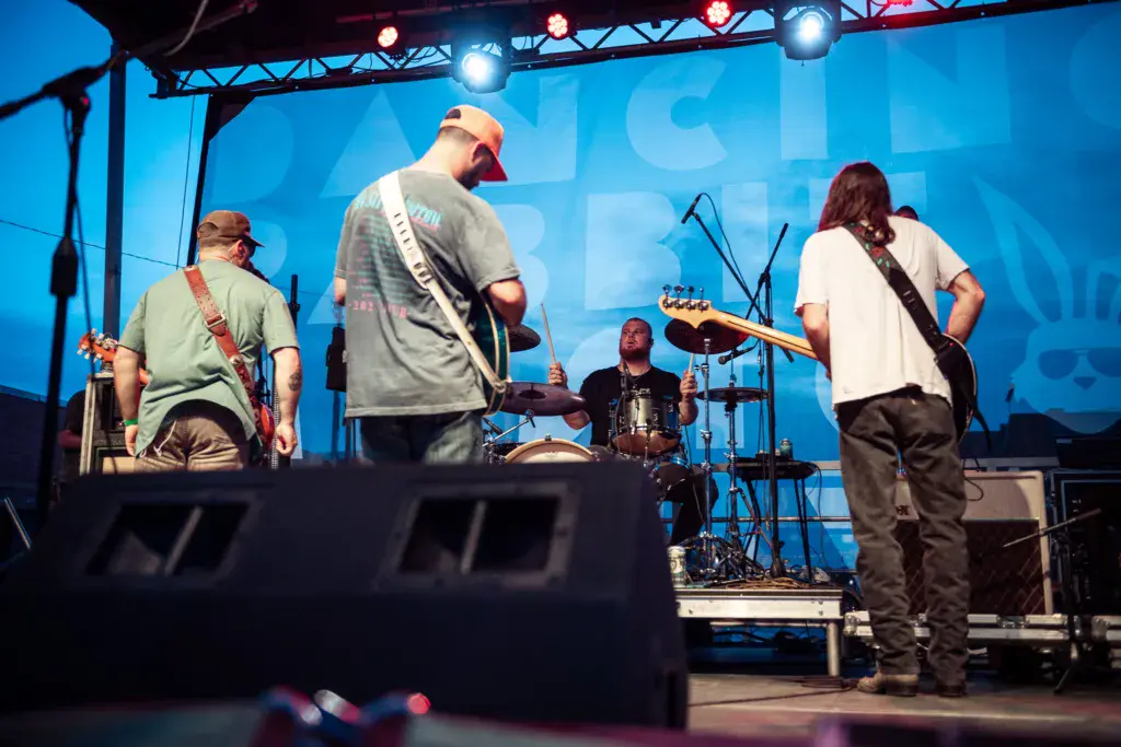A band performs on stage with blue lighting, featuring multiple guitarists and a drummer.