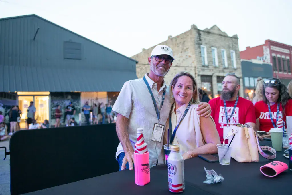 Festival volunteers and staff stand at a table with beverages at the Dancing Rabbit Music Festival outdoor venue.