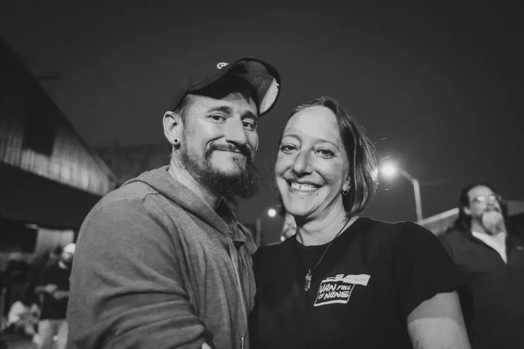 Two people smiling at the camera at an outdoor festival venue at night.