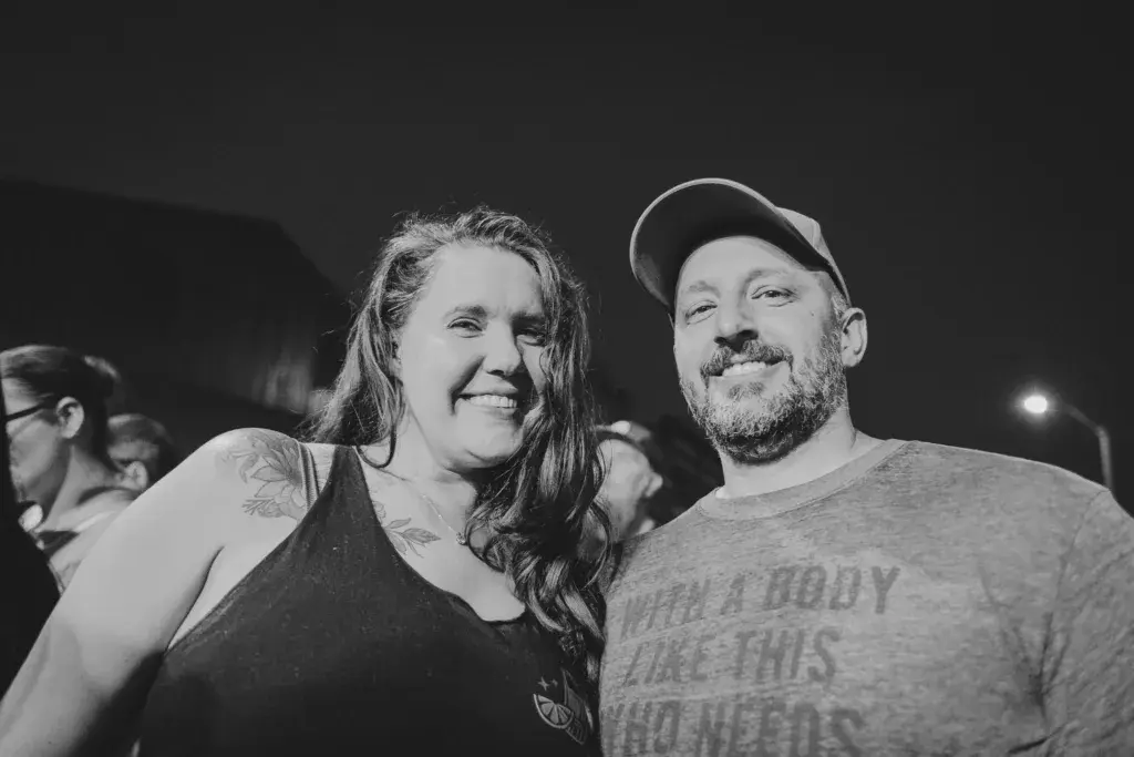 Two smiling people pose together at an outdoor night event in black and white.