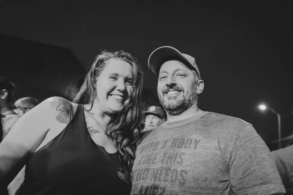 Two people smiling at the camera during the Dancing Rabbit Music Festival at night.