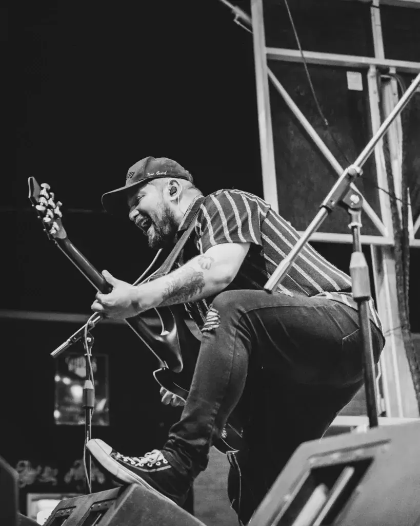A musician with a beard and cap plays guitar on stage during a night performance in black and white.