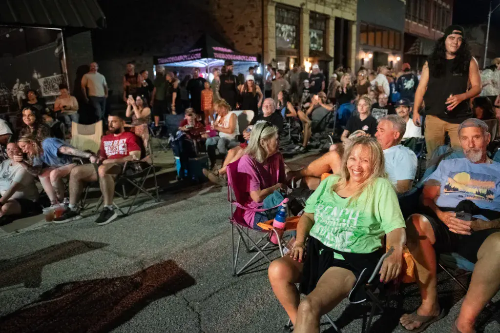 Evening crowd seated on the street at Dancing Rabbit Music Festival with stage and venue buildings visible.