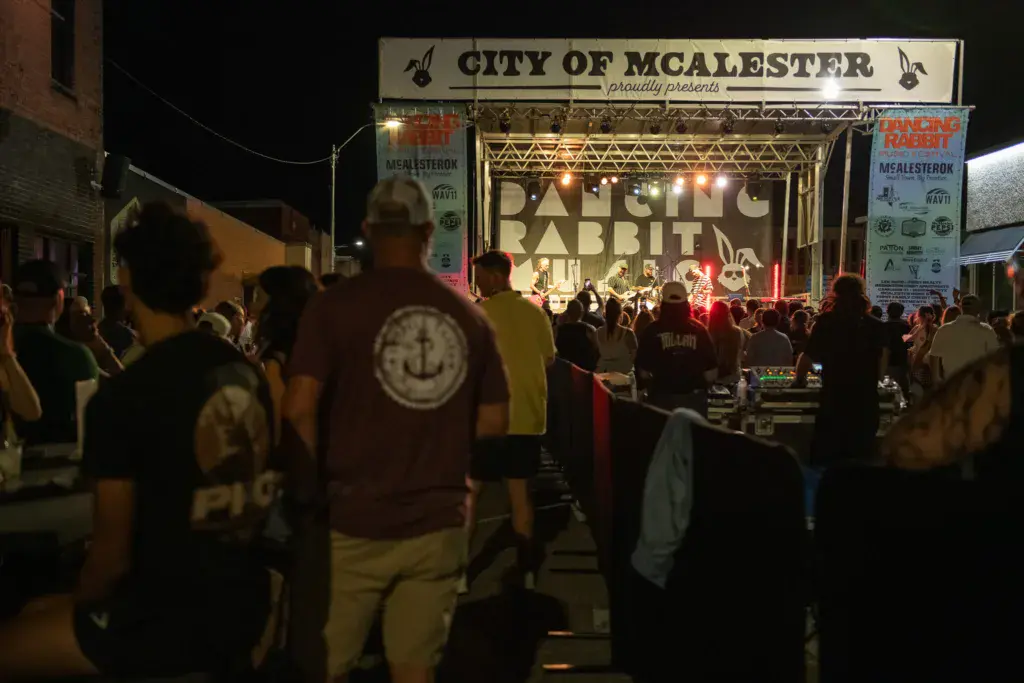 Night scene of a crowd gathered in front of an illuminated stage at the Dancing Rabbit Music Festival in McAlester.