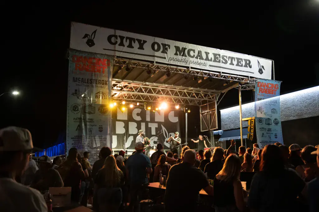 A band performs on an illuminated stage at night while a large crowd watches in front of sponsor signage.