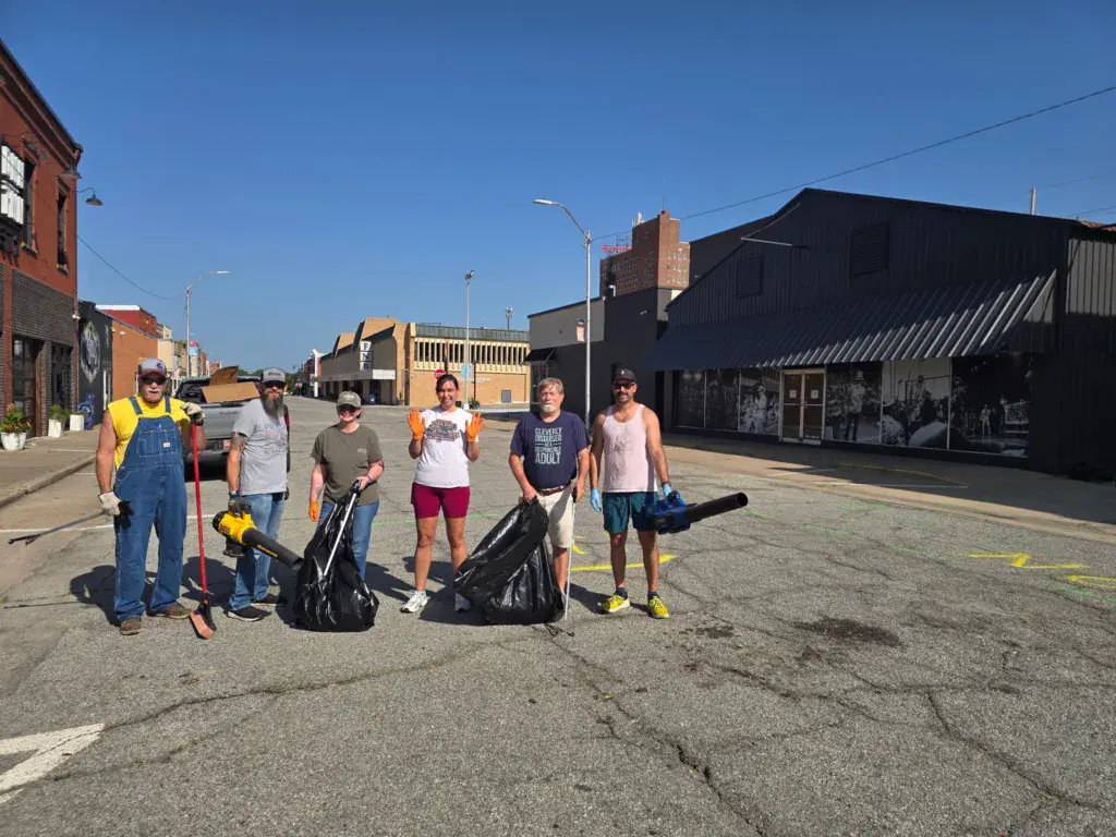 A group of volunteers stand together in an urban street holding trash bags during a cleanup effort.