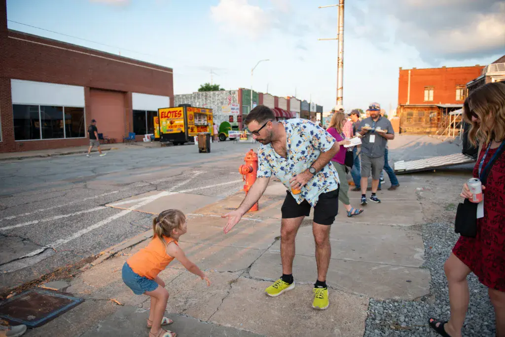 A man and child play with a jump rope at an outdoor festival venue in an empty parking lot.