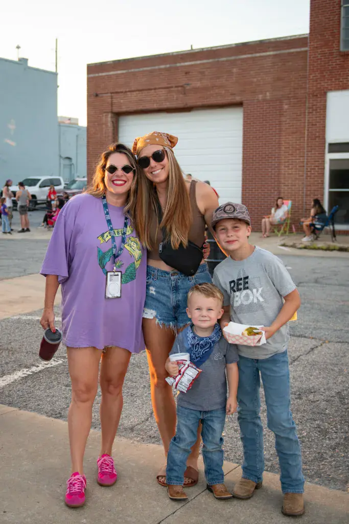 Four festival attendees posing together in a parking lot venue area during daytime.