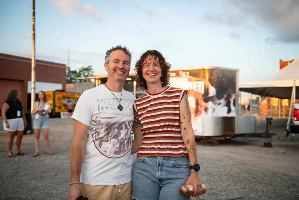 Two smiling people posing together at an outdoor festival venue during golden hour.