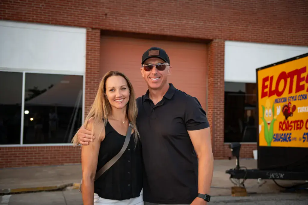 Two people smiling at the camera in front of a brick building with festival signage.