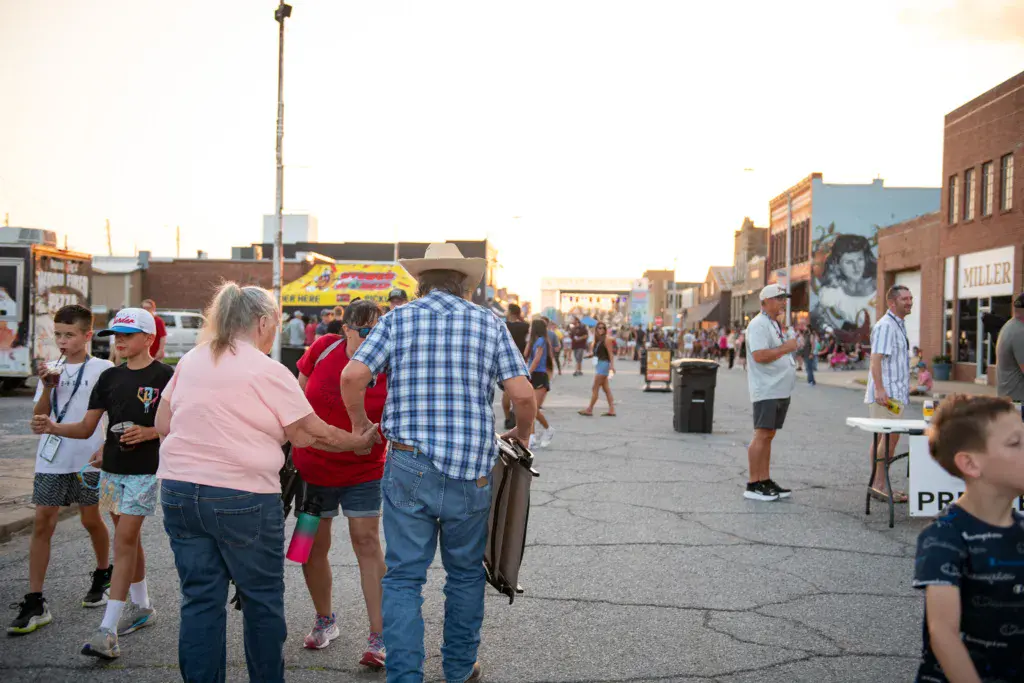 Festival attendees walking and gathering in a paved outdoor venue lined with brick buildings during daytime.