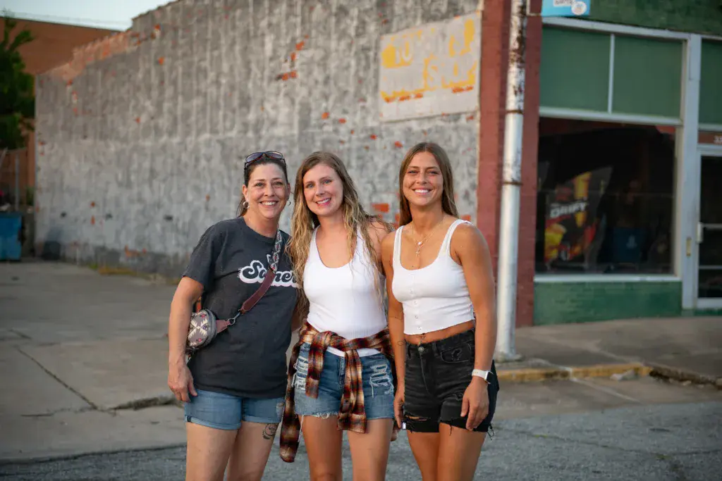Three people smiling at the camera in front of a weathered building at the festival venue.