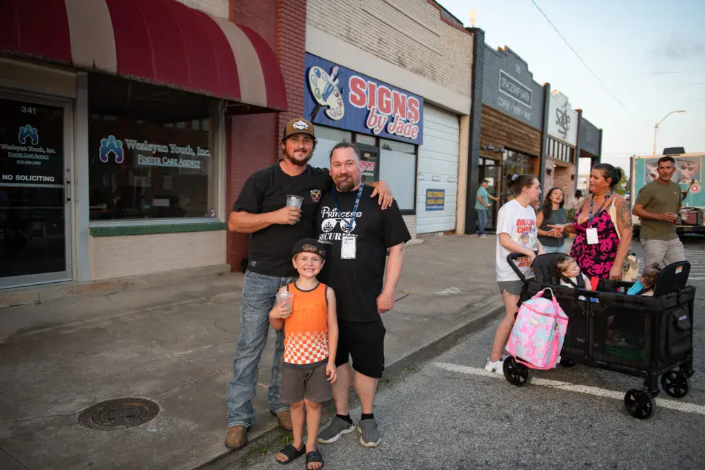 Festival attendees and staff pose together on a street lined with storefronts and signage.