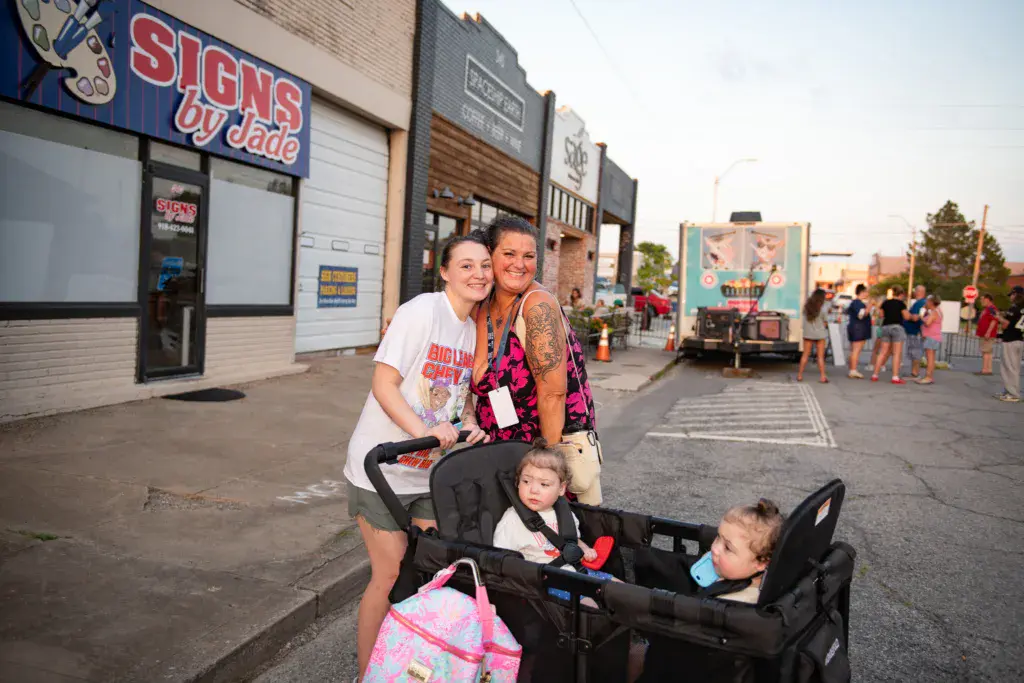Two adults and two young children pose together at a festival venue with storefronts in the background.