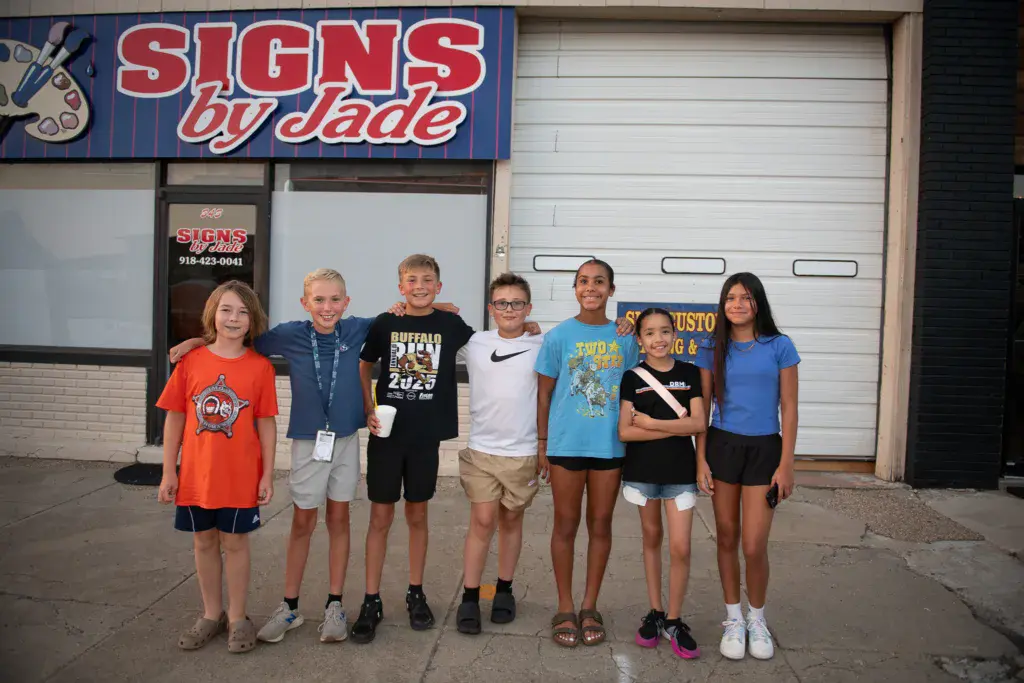 A group of seven young people posing together in front of a sign shop storefront at the festival.