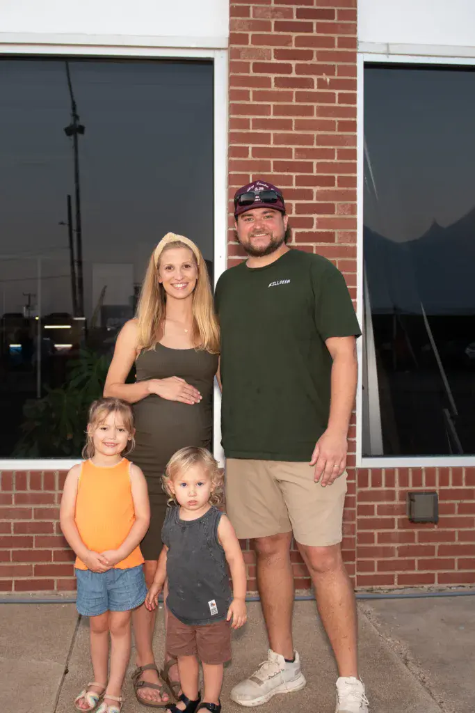 Family of four posing together in front of a brick building with large windows.
