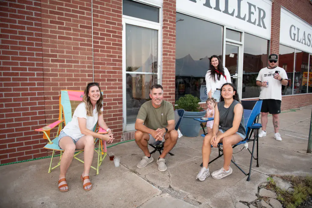Festival attendees relax in camping chairs outside a brick storefront during Dancing Rabbit Music Festival.