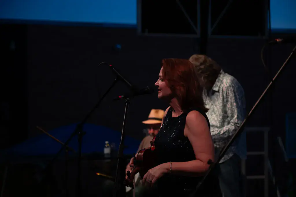 A performer with red hair plays guitar at a microphone on stage during evening twilight at the festival.