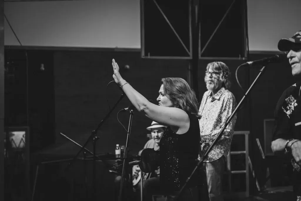 A performer sings at a microphone on stage with band members behind her at an outdoor music festival.