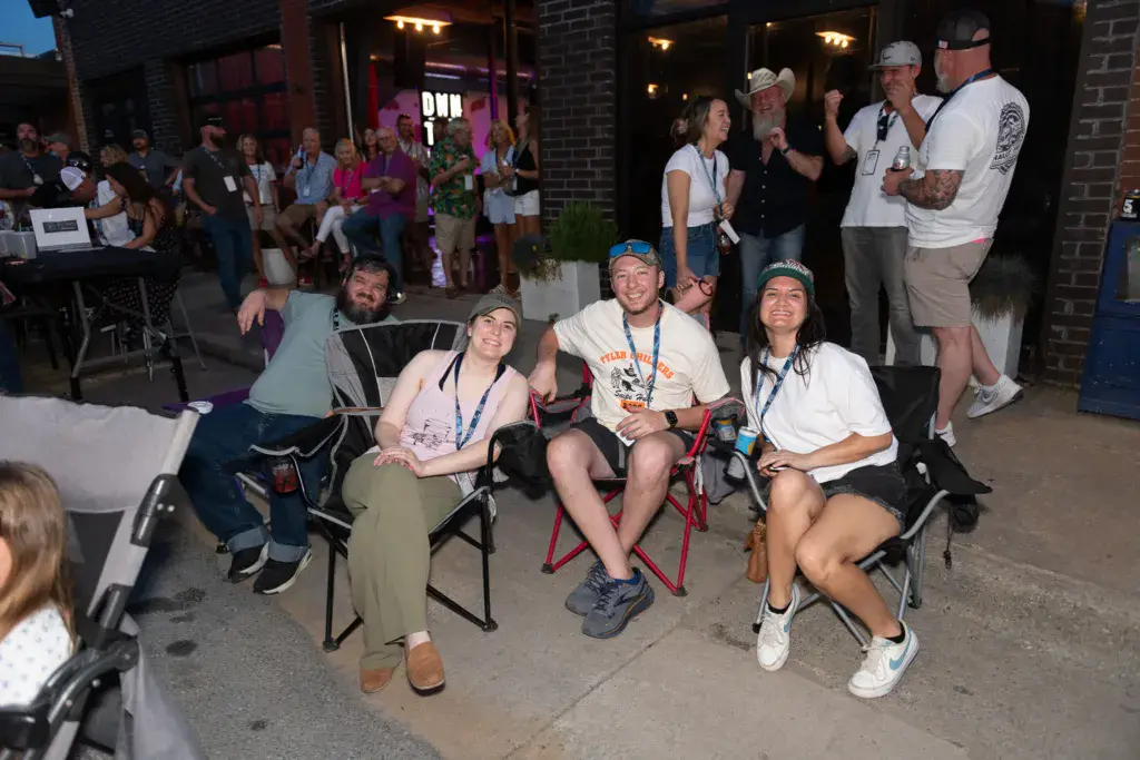 Festival attendees sit and stand together in a brick venue courtyard at evening with warm lighting.