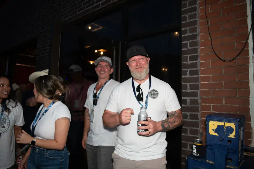 Festival staff members wearing lanyards and white t-shirts socialize indoors by a brick wall at night.