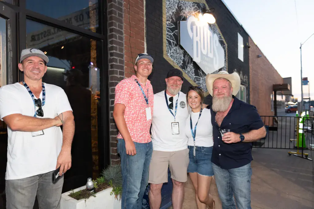 A group of five people wearing festival badges stand together outside a brick venue building at the Dancing Rabbit Music Festival.