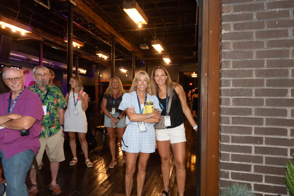 Group of festival attendees wearing lanyards gathered indoors under warm lighting near a brick wall.