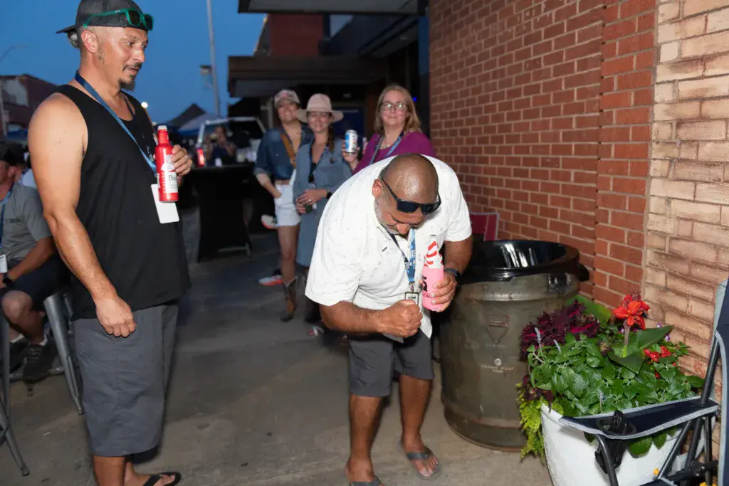Festival attendees gather in an alley by a brick wall, holding drinks during an outdoor music event.