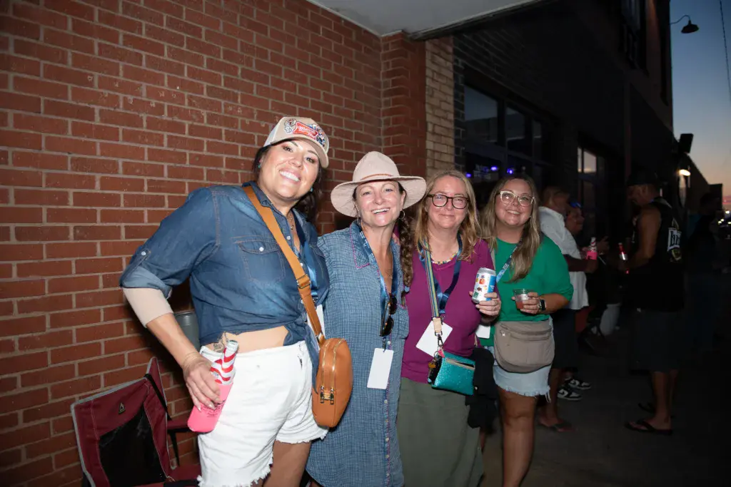 Four festivalgoers smile together against a brick building exterior at the Dancing Rabbit Music Festival.