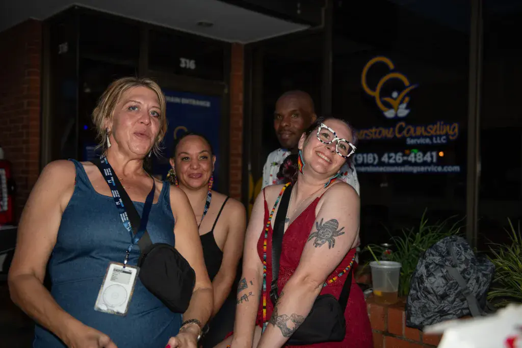 Four people wearing festival lanyards stand together outside a brick building at night.