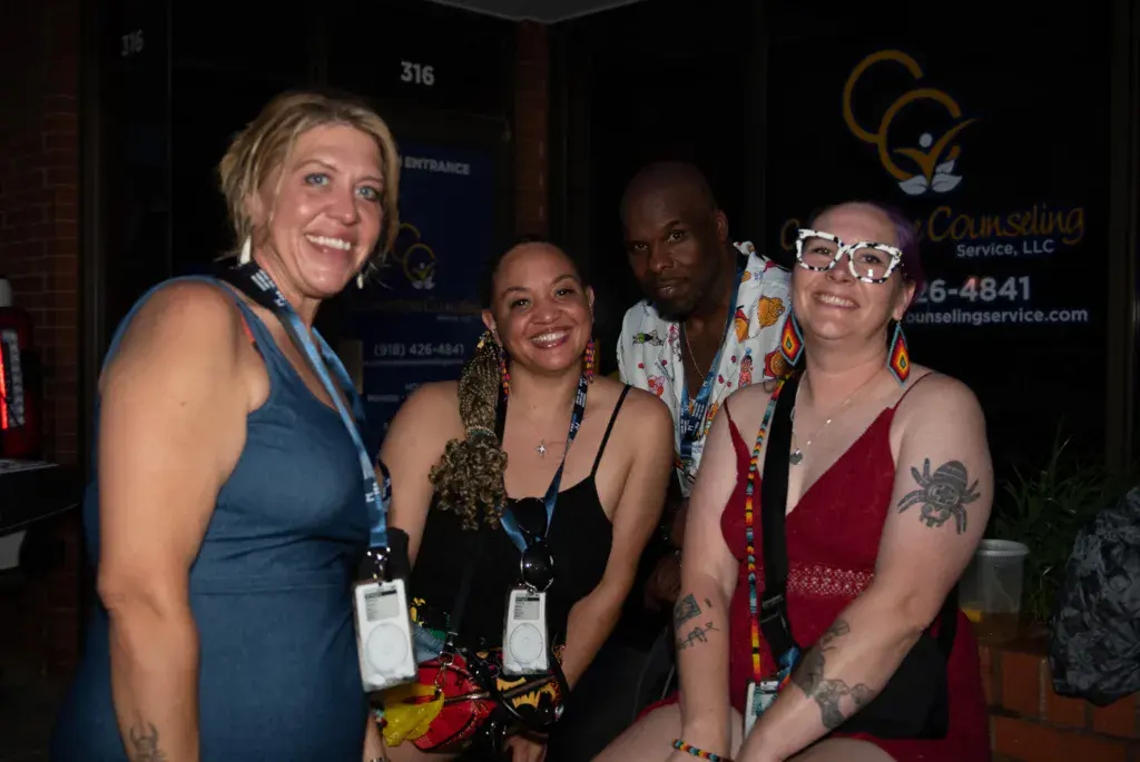 Five people wearing festival lanyards smile for a photo together in an indoor venue.