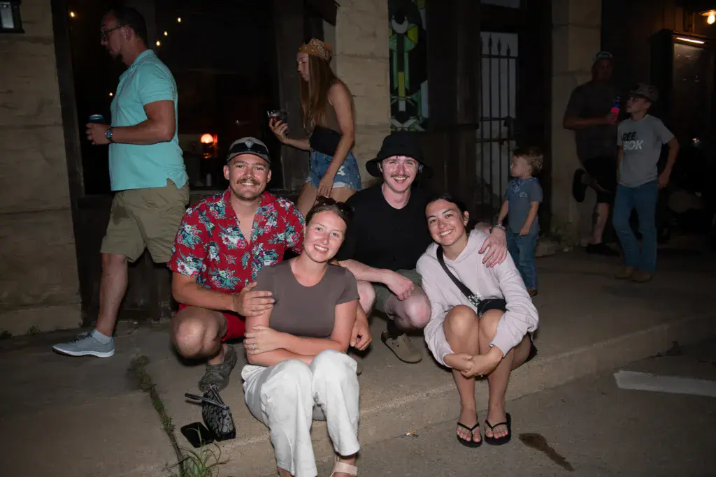 A group of festival attendees smile for the camera while gathered together at night near a venue building.