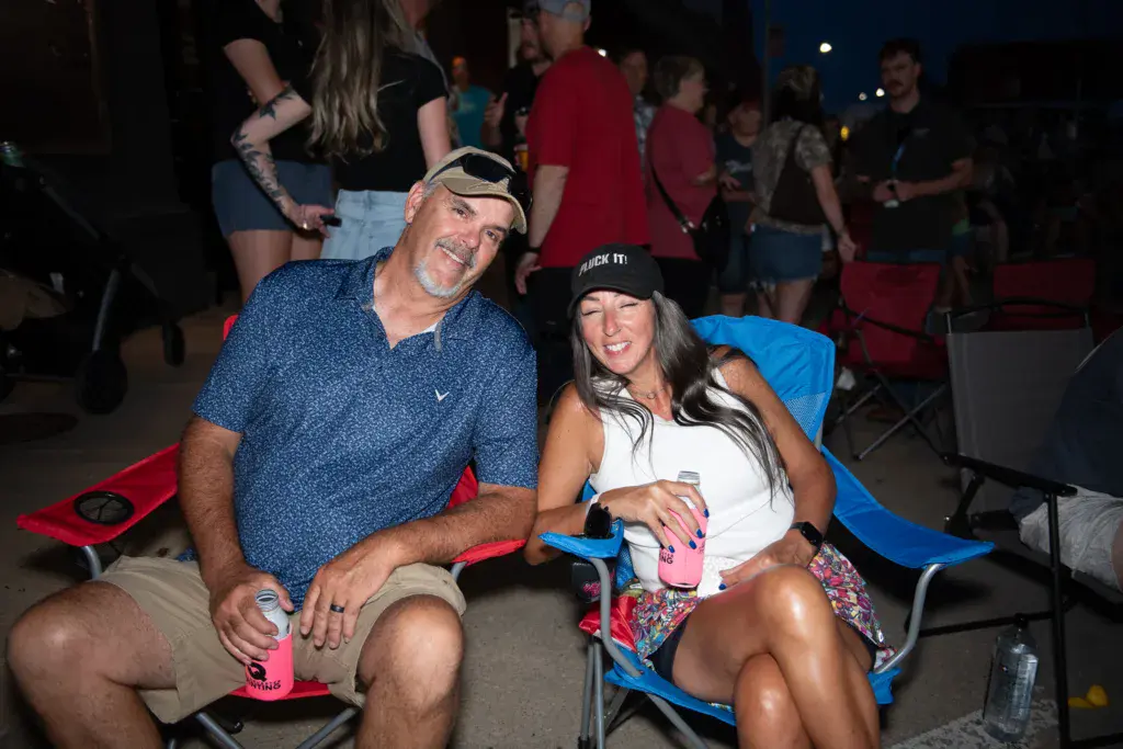 Two festival attendees smile while sitting in lawn chairs at an evening outdoor event.