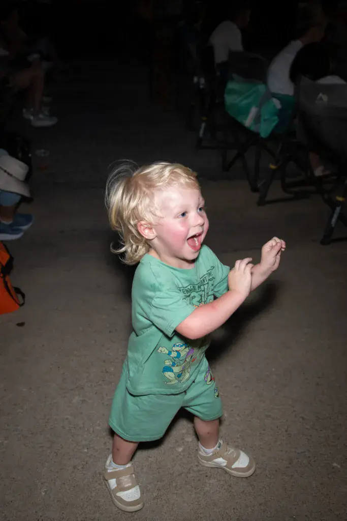 A young child in a green shirt dances joyfully at the Dancing Rabbit Music Festival.