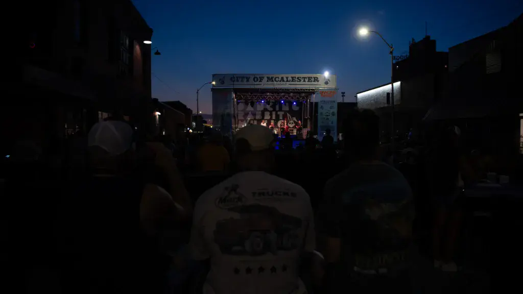 Evening view of a stage with crowd silhouettes and signage reading 'City of McAlester' under a twilight sky.