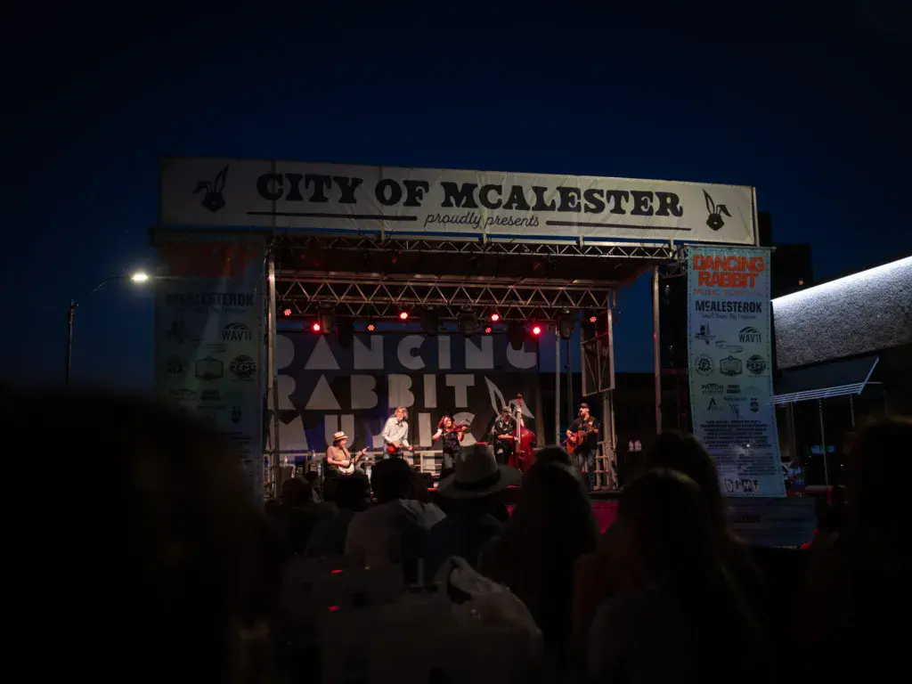 A band performs on an outdoor stage at night with a crowd watching below.