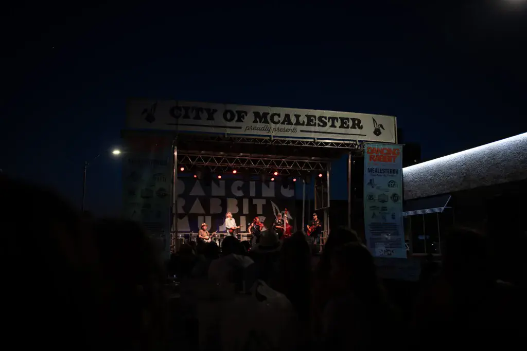 A band performs on an illuminated stage at night with crowd silhouettes in the foreground at Dancing Rabbit Music Festival.