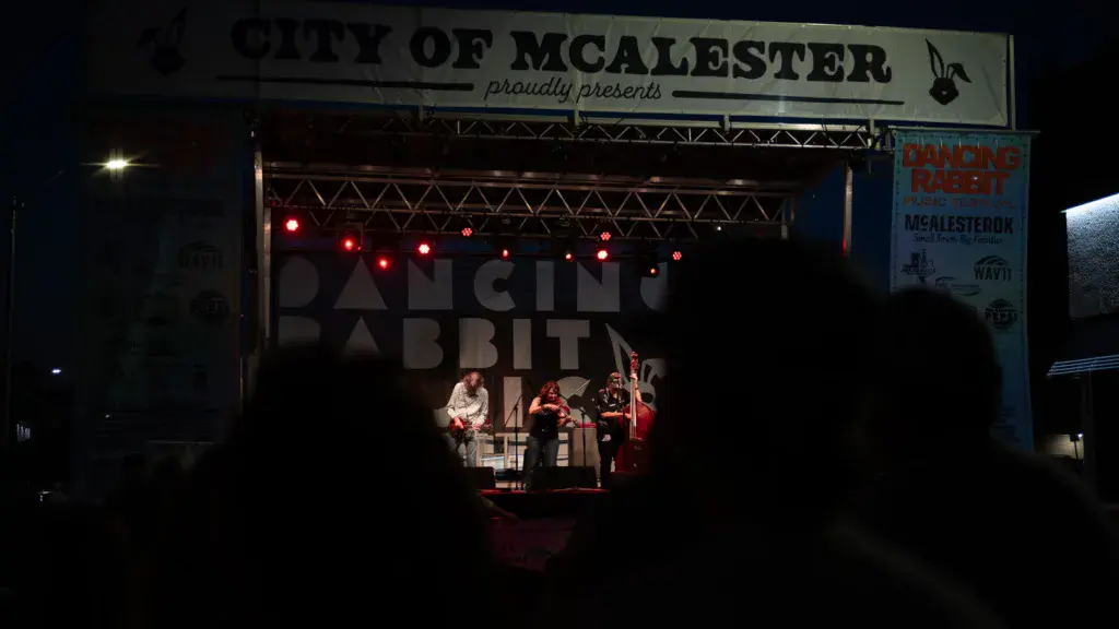 Band performing on an illuminated stage at night with crowd silhouettes in foreground and festival signage visible.