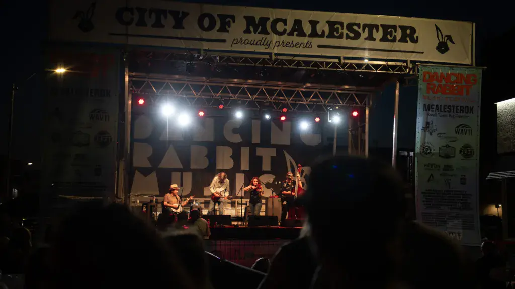 A live band performs on an illuminated stage at Dancing Rabbit Music Festival with crowd members visible in silhouette.