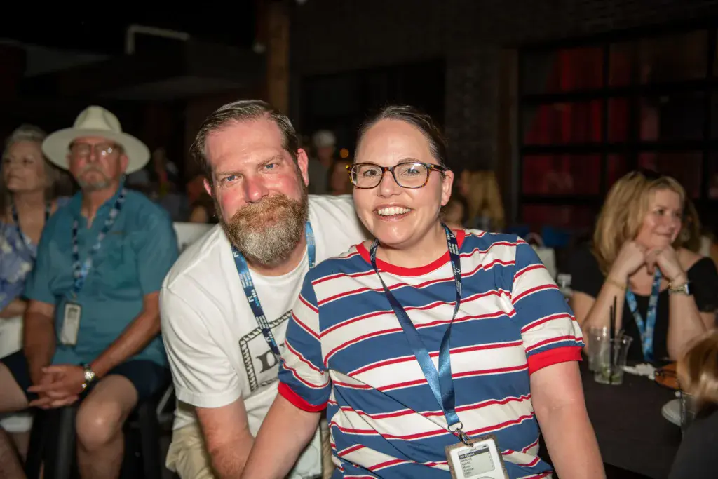 Festival attendees wearing credential badges smile at an indoor venue gathering.