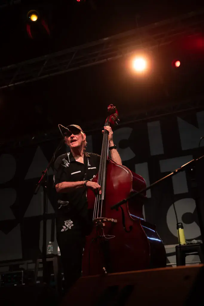 A musician performs on stage at night playing a red cello under warm stage lighting.