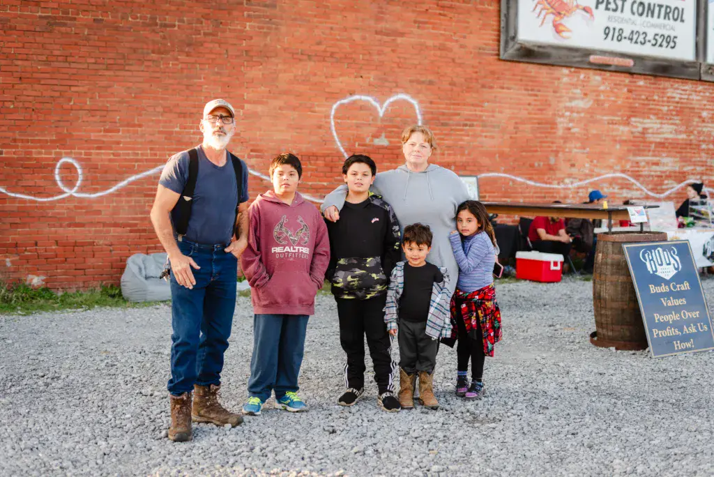 A group of six people posing together in front of a red brick wall with chalk drawings at an outdoor venue.