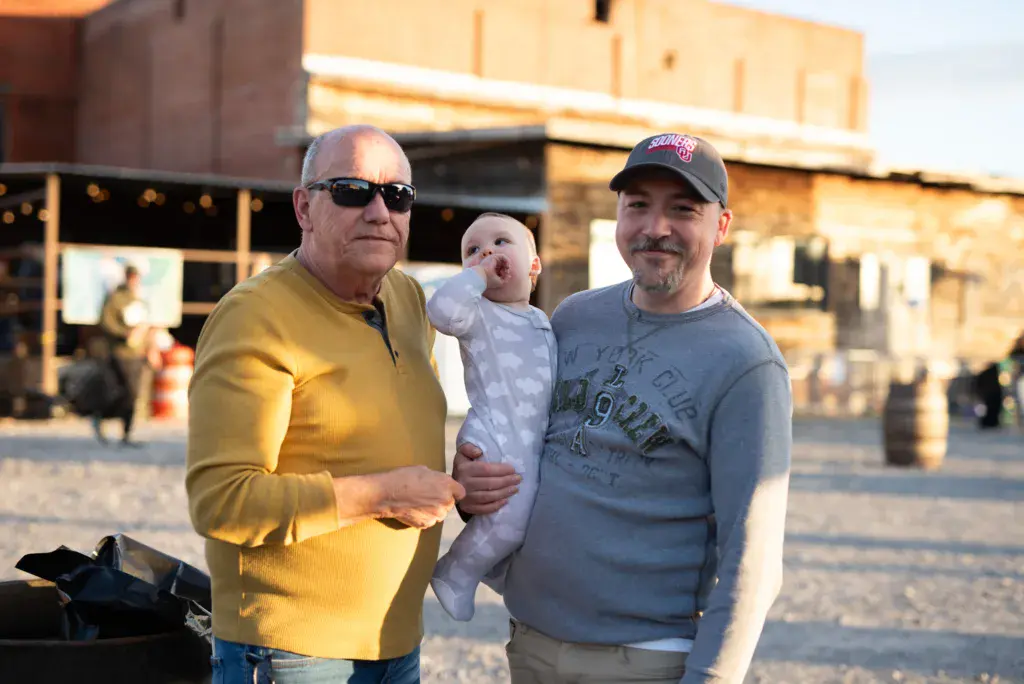Two men and an infant stand together in a festival venue courtyard during golden hour.