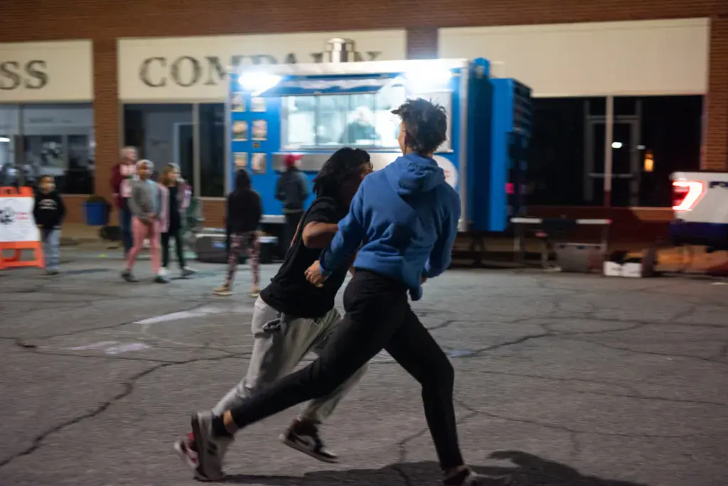 Two people run together in front of a blue food truck at an outdoor festival venue.