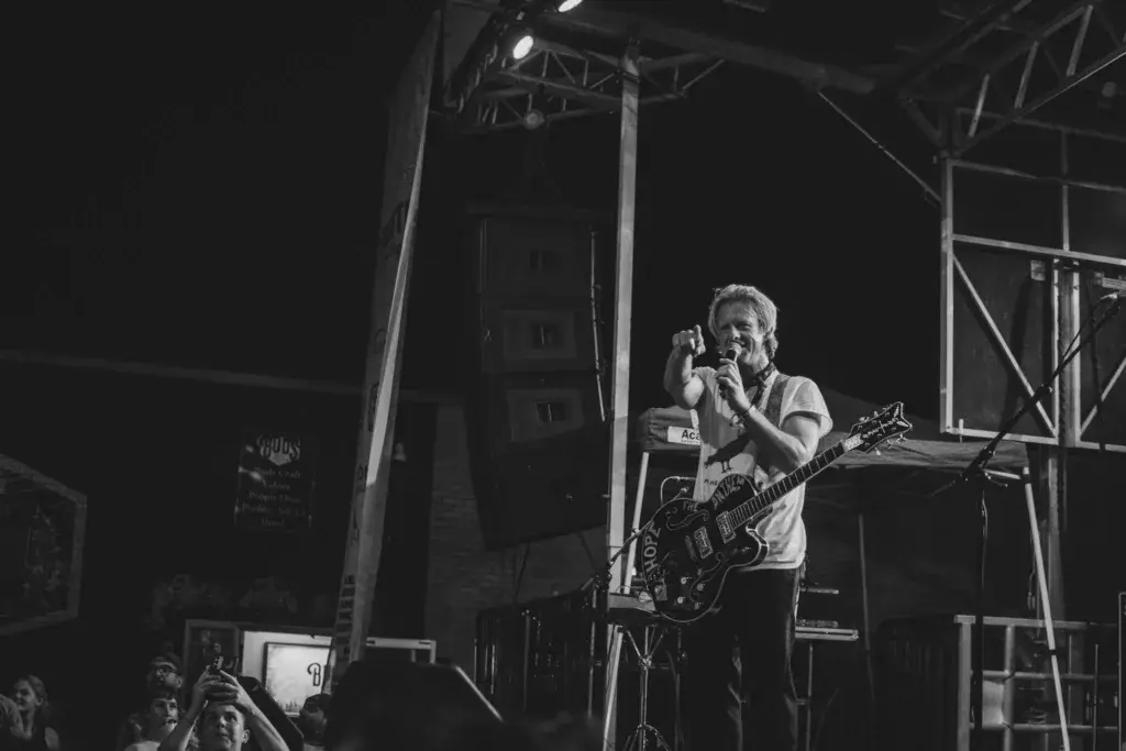 A guitarist and singer performs on stage at night with amplifiers and stage lighting visible.