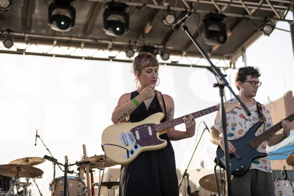 Two musicians perform on stage with guitars under a lit canopy at an outdoor music festival.